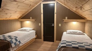 A small, cozy attic bedroom with two single beds, wooden beams on the ceiling, and a black door. - The Sandtown 3 bedroom Cabin (Vian)