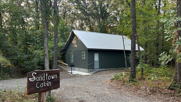 A cabin with a gravel path leading to it, surrounded by trees. - The Sandtown 3 bedroom Cabin (Vian)