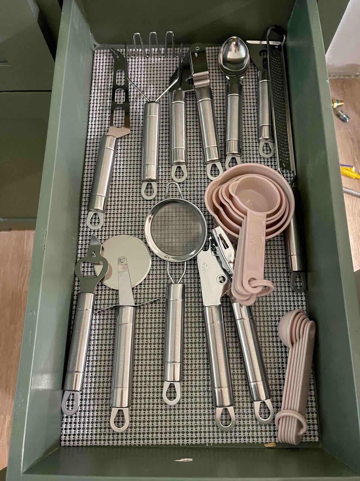 A drawer with various kitchen utensils and tools, including spatulas, tongs, and a strainer.