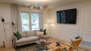 Una sala de estar moderna con un sofá, dos sillas de madera, una mesa de centro y un televisor montado en la pared.