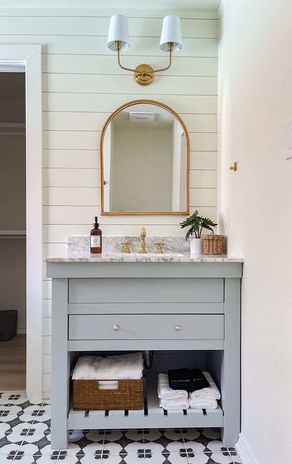 A bathroom with a white vanity, a gold-framed mirror, and a two-light fixture above the mirror.