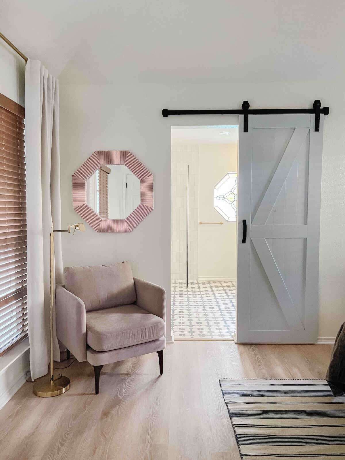 A room with a light-colored sofa, a round mirror with a striped frame, a floor lamp, a striped rug, and a sliding barn door.