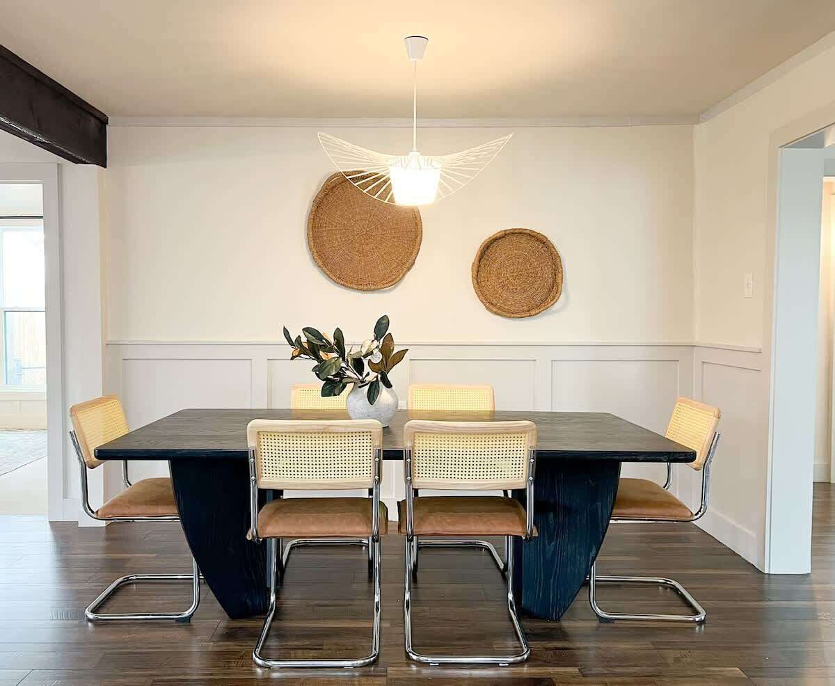Un coin repas comprenant une table rectangulaire, quatre chaises, un luminaire suspendu et deux éléments de décoration murale en fibres tressées.