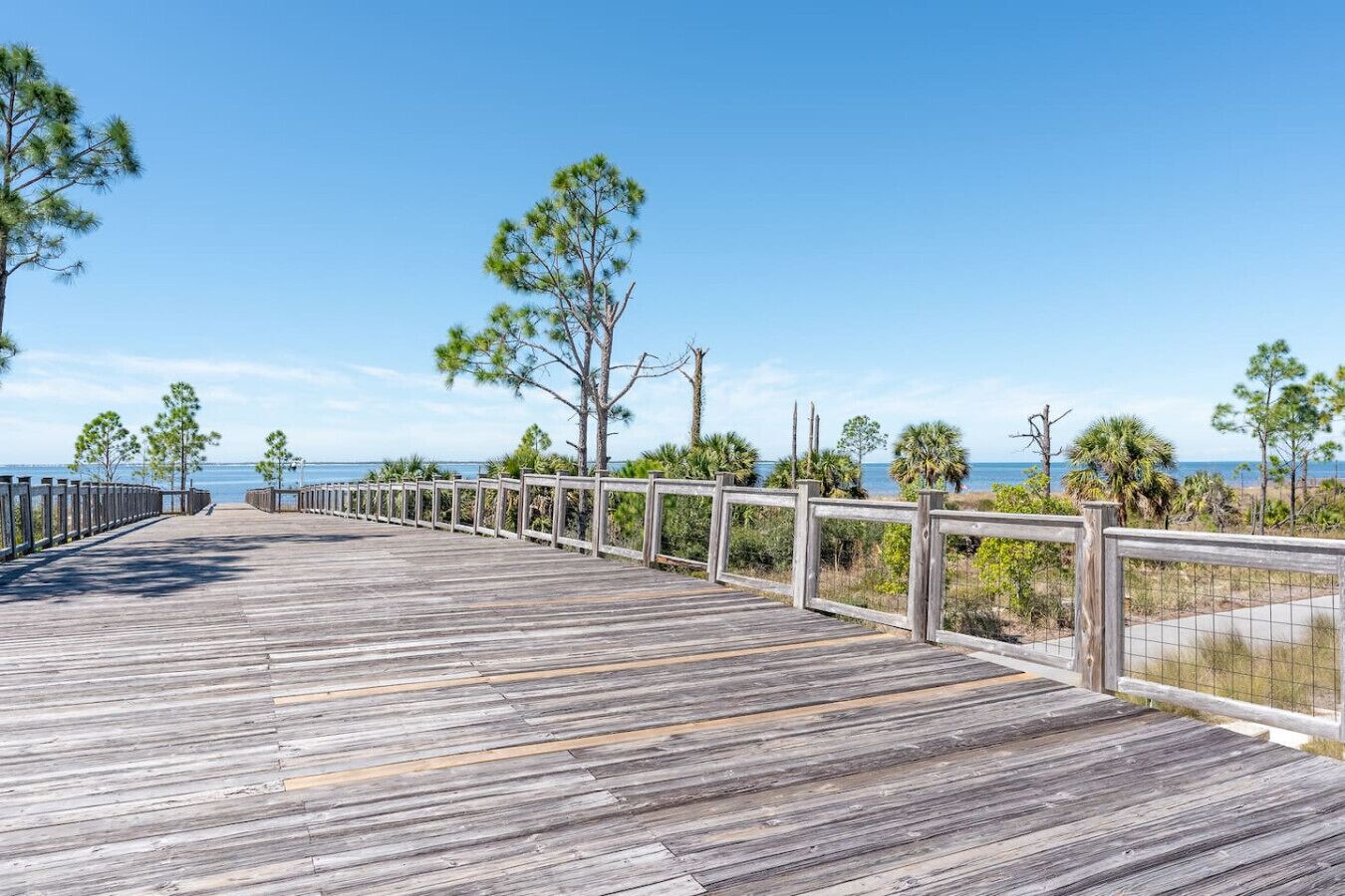 A wooden boardwalk leading to a beach with a clear view of the ocean.