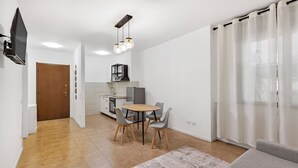 A modern living room with a sofa, a dining table with chairs, a kitchen area with cabinets and a refrigerator, and a TV mounted on the wall. - Alessia's Flat - Borgo Palazzo 005 (Bergamo)