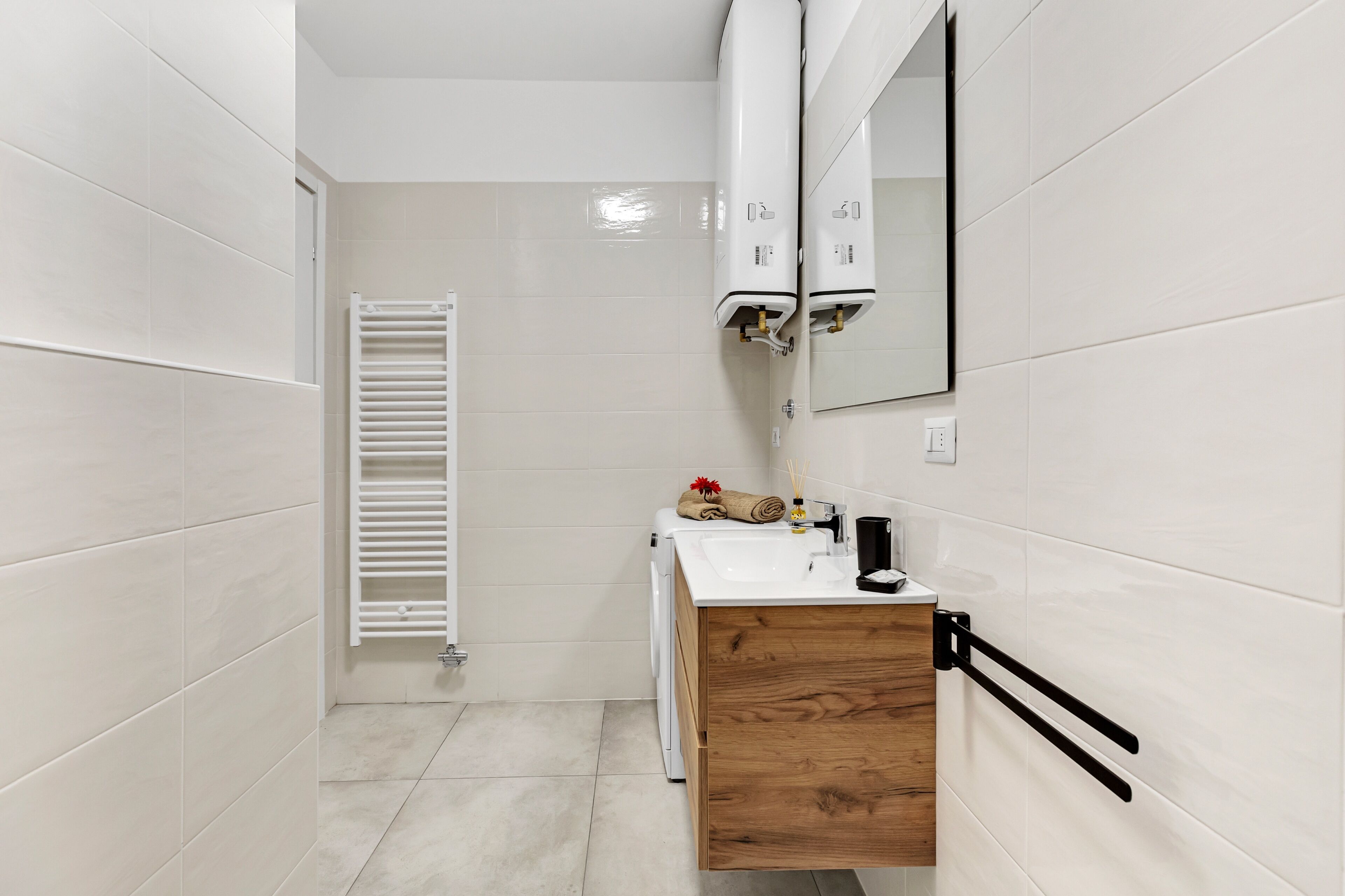 Une salle de bain moderne avec des carreaux blancs, un meuble-lavabo en bois, un évier, un miroir et un porte-serviettes.