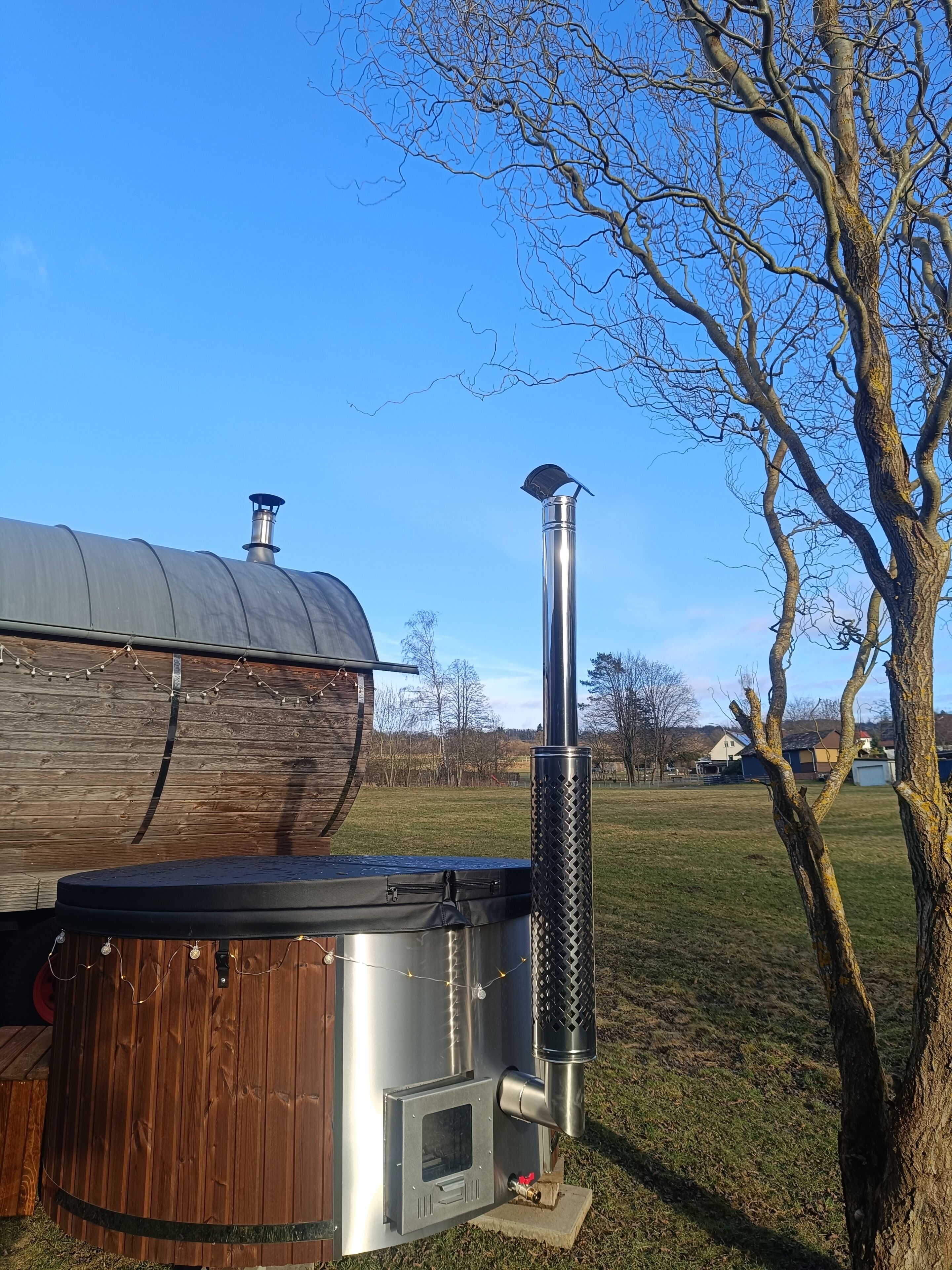 Un entorno rústico al aire libre con una estructura de madera, una chimenea de metal y un árbol.