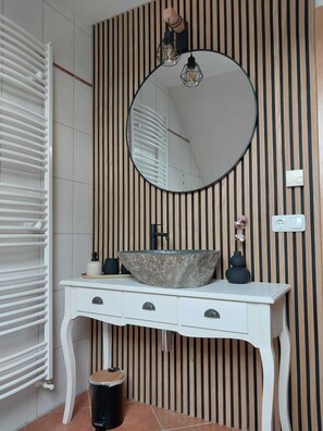 Une salle de bain avec un meuble-lavabo blanc, un miroir rond, un évier en pierre et un mur à rayures.