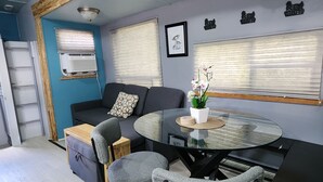 Una sala de estar moderna con una mesa de comedor de vidrio, sillas tapizadas de color gris, un sofá oscuro y una viga de techo de madera.
