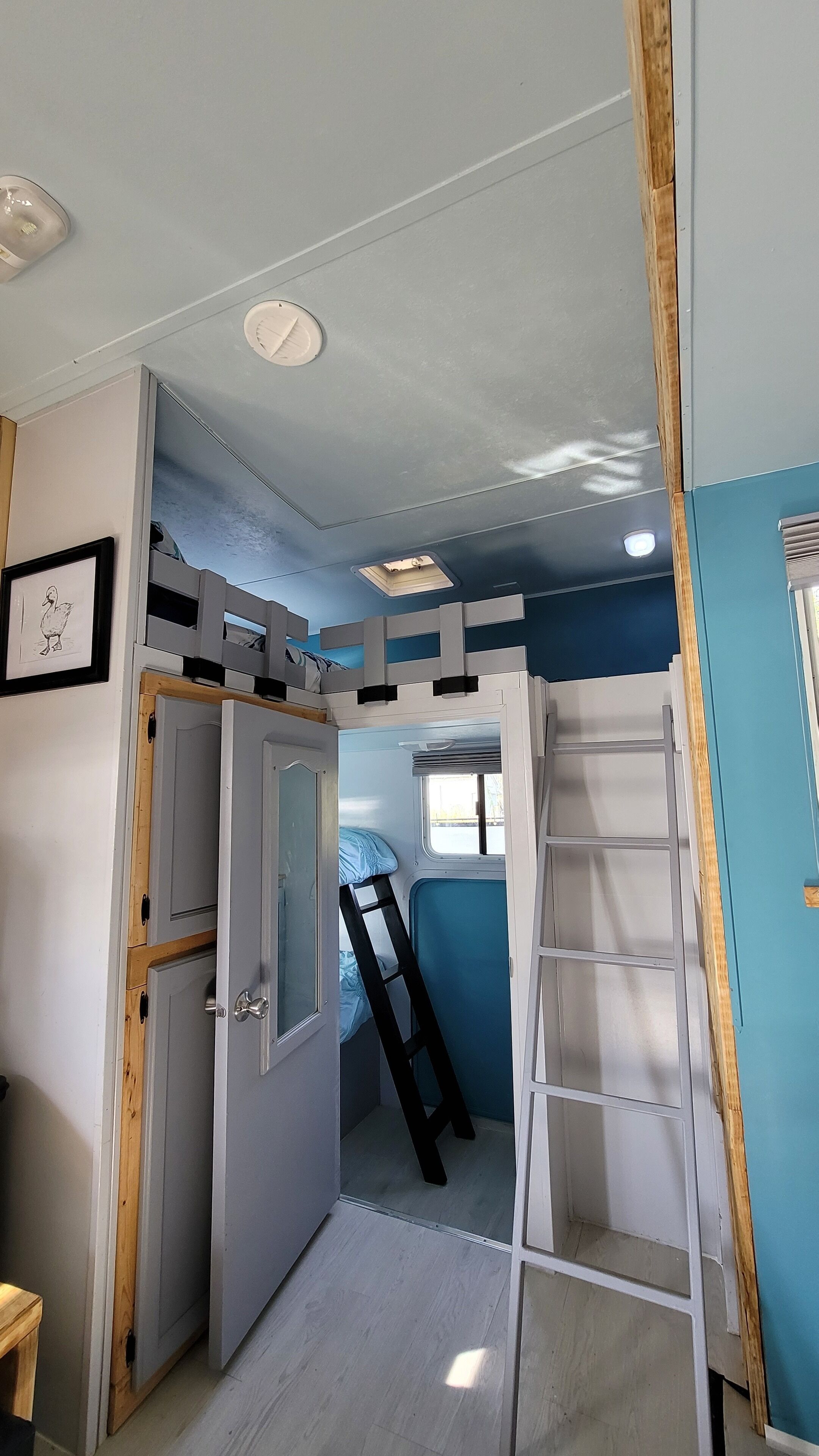 Habitación pequeña con literas, una escalera y una puerta que da a otro espacio.