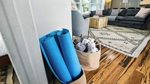A living room with a dark grey sofa, a patterned rug, and a wooden coffee table. Blue yoga mats and rolled towels are visible. - Tranquil Waterfront • Enclosed pool • Kayaks (Oakland Park)