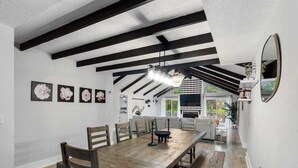 A dining area with a long wooden table, black beams on the ceiling, and framed artwork on the wall.