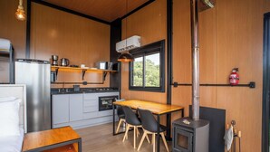 Cocina compacta con estufa de leña, una mesa de comedor y vistas al exterior a través de una ventana.
