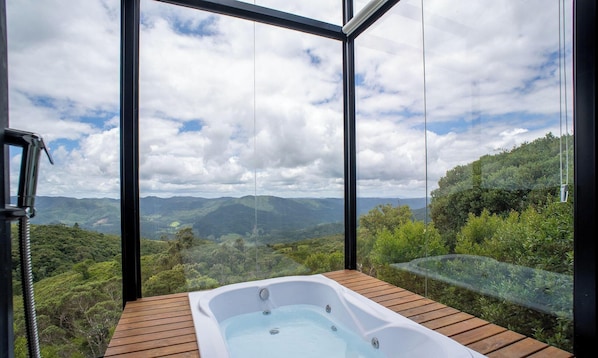 A hot tub on a wooden deck with a view of a mountainous landscape through large windows.