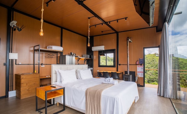 A modern hotel room with a large bed, wooden walls, a small desk, and a window with a view of the outdoors.