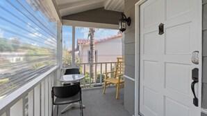 Een balkon met een tafel en stoelen, een witte deur en uitzicht op een gebouw en een palmboom.