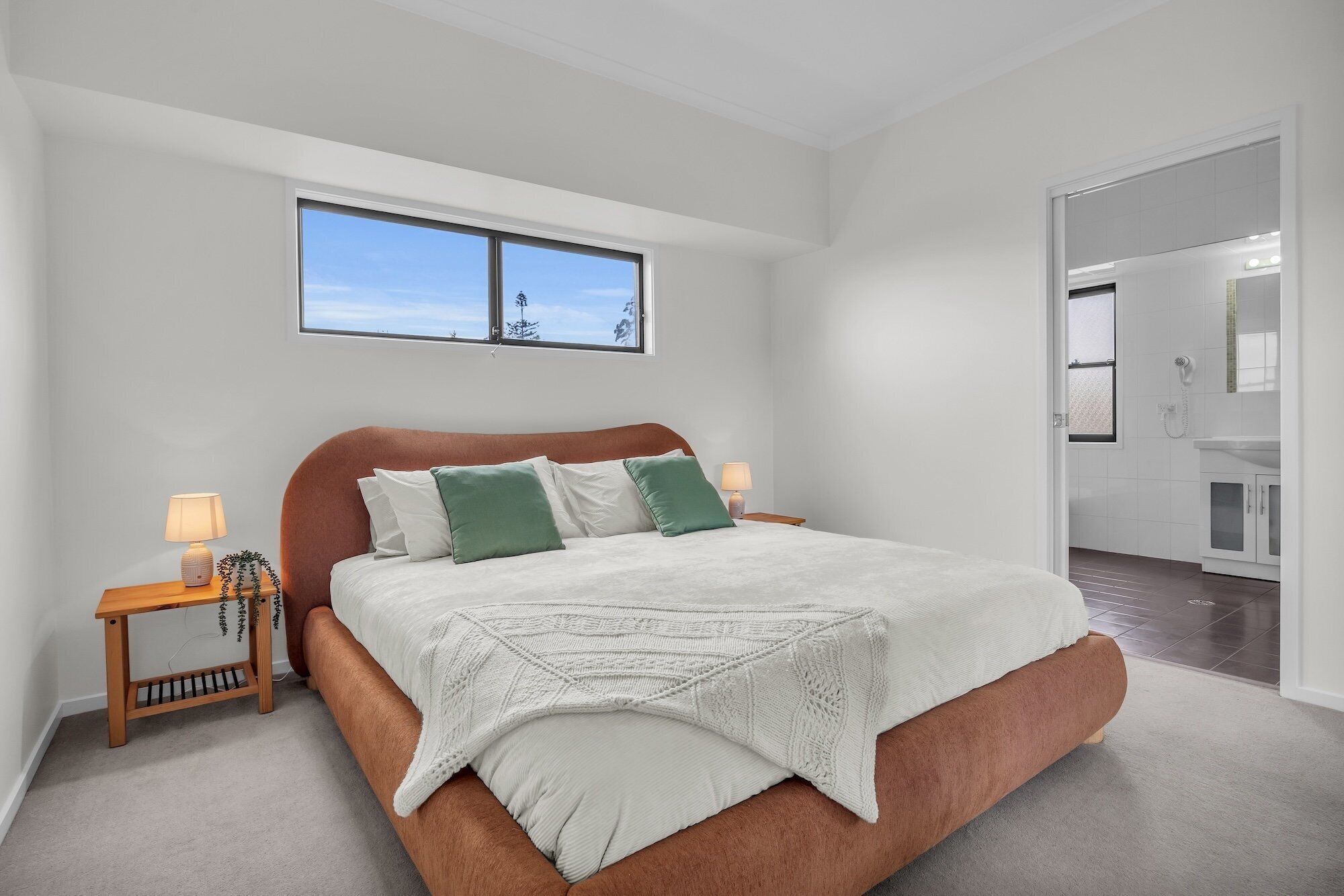 A bedroom with a bed, a nightstand, a window, and a bathroom visible through an open door.
