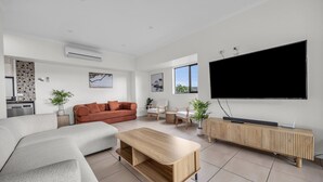 A modern living room with a sofa, a coffee table, a TV, and a dining area. - Saltwater Apartments - 2 Bedroom (Eden)