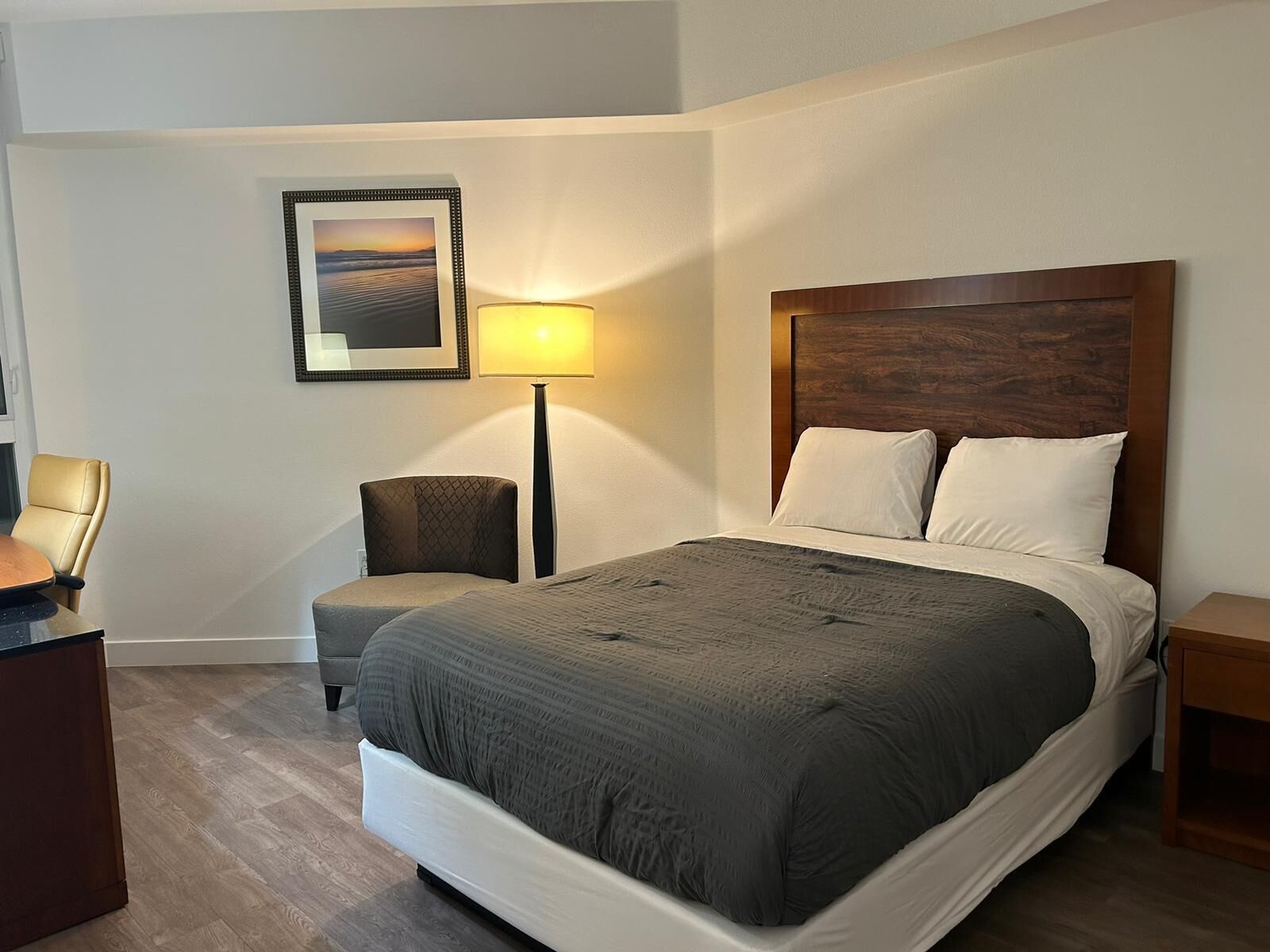 Hotellihuone, jossa on suuri sänky, työpöytä, tuoli, lamppu ja seinällä oleva kehystetty kuva.