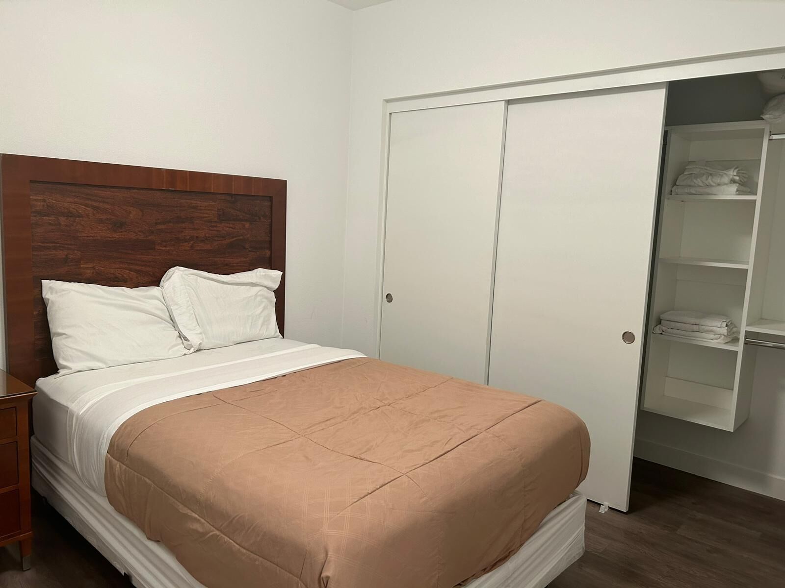 Un dormitorio con cama, cabecera de madera, armario blanco y armario con ropa doblada.