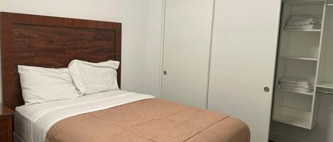 Un dormitorio con cama, cabecera de madera, armario blanco y armario con ropa doblada.