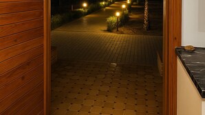 A hallway with a wooden door leading to a paved outdoor area at night, illuminated by pathway lights. - Villa with swimming pool not overlooked (Marrakech)