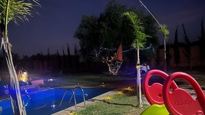 A swimming pool with a slide, surrounded by grass and trees, and string lights. - Villa with swimming pool not overlooked (Marrakech)