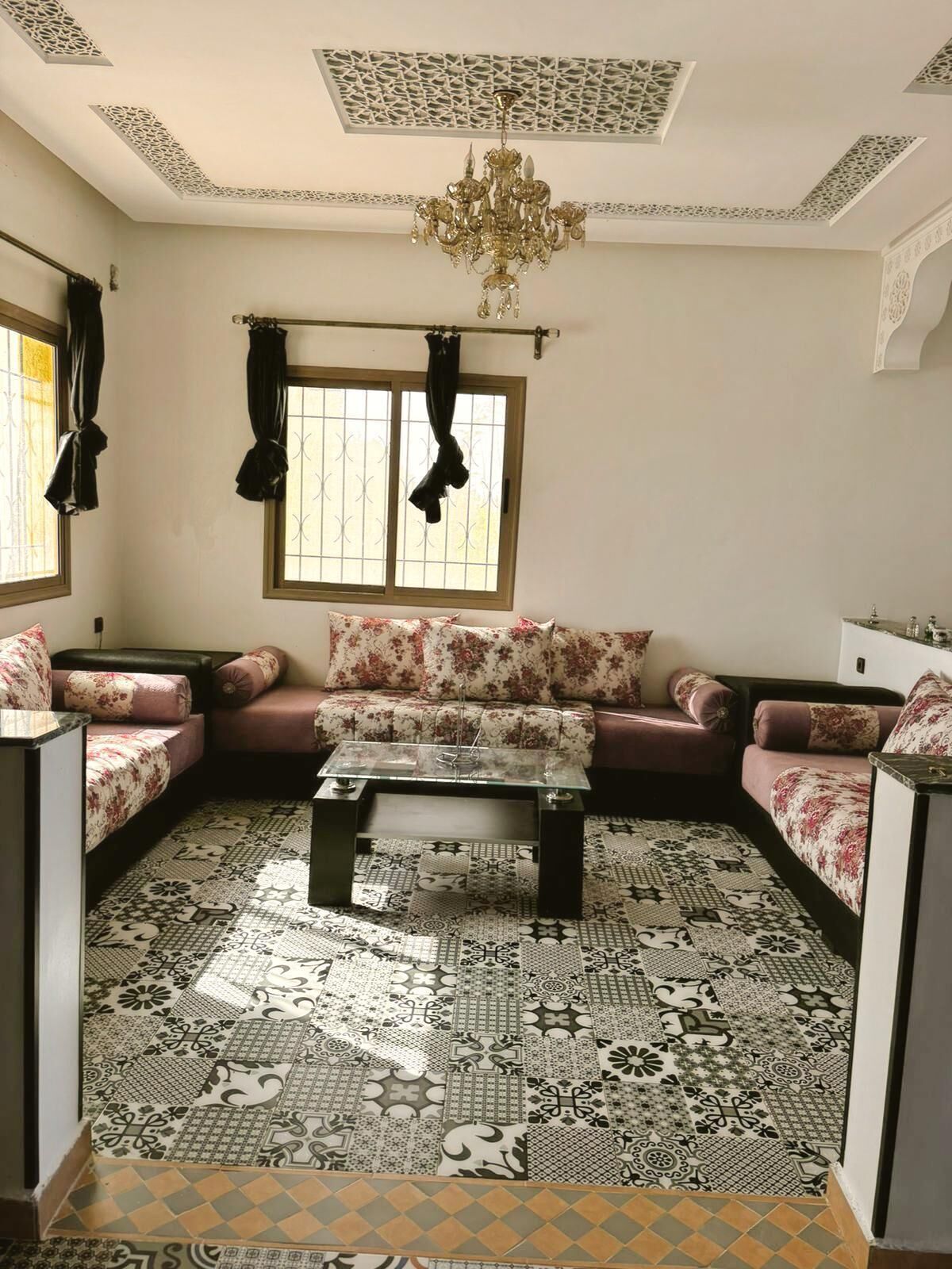 A living room with a patterned floor, a sofa set, a coffee table, and a chandelier.