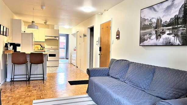 Ein modernes Wohnzimmer mit einer Couch, einem Essbereich mit Stühlen, einer Küche und einem Flur, der zu einer Tür führt.