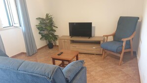 Ett vardagsrum med en soffa, en fåtölj, ett soffbord, en tv som står på ett träställ och en krukväxt.