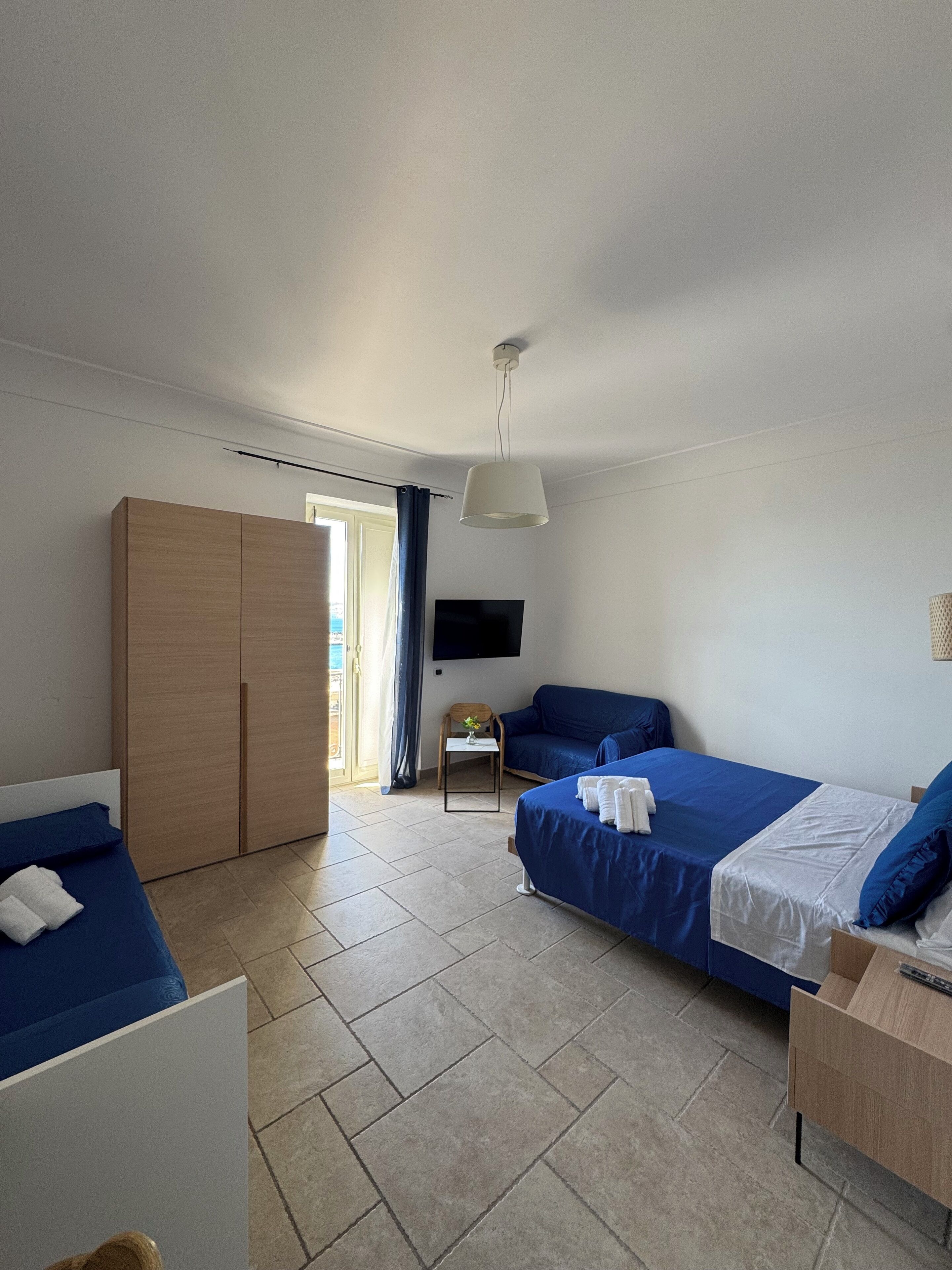 A hotel room with two beds, a TV, a wardrobe, and a small table with a plant.