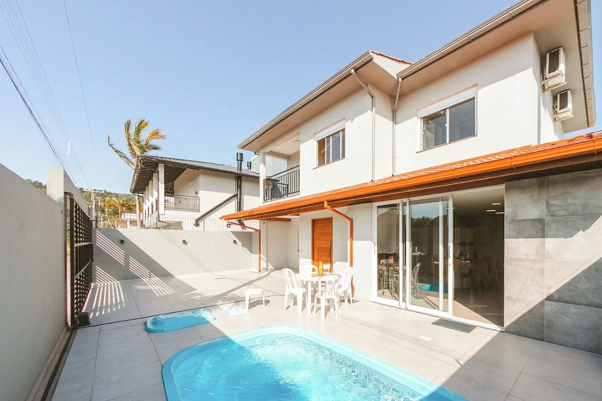 Una casa moderna de dos pisos con piscina, mobiliario exterior y un patio cubierto.