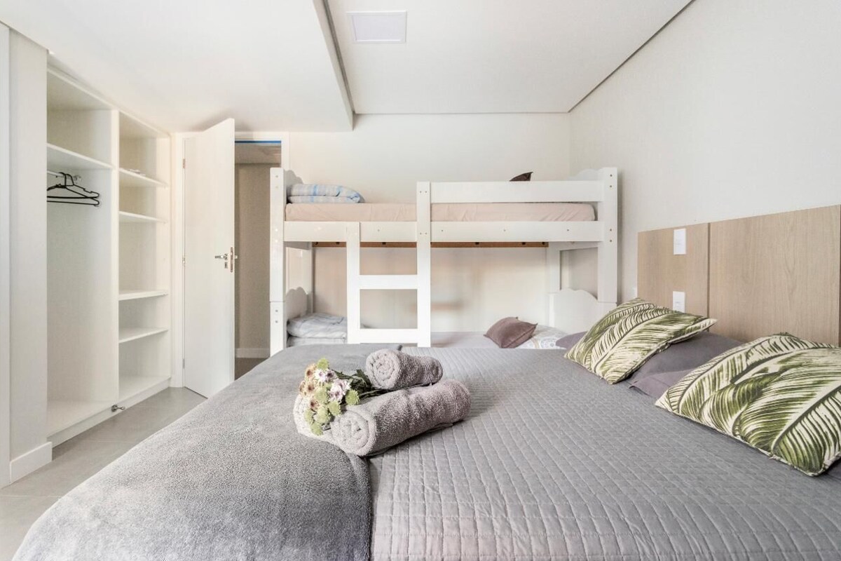 A bedroom with bunk beds, a wardrobe, and a bed with rolled towels and a bouquet.