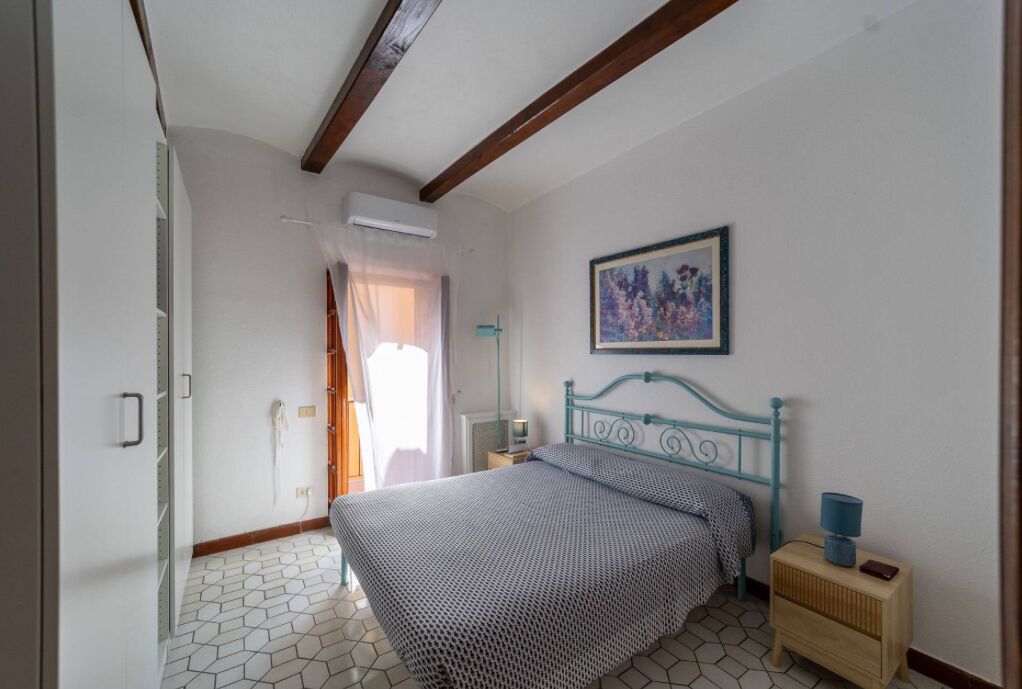 Ein Schlafzimmer mit Bett, Nachttisch, einem Bild an der Wand und einem Fenster mit Vorhängen.
