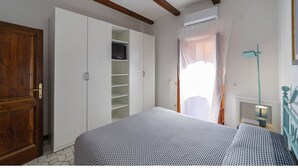 Un dormitorio con cama, armario, televisor y ventana con cortinas.