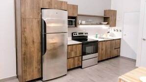 A modern kitchen with wooden cabinets, a stainless steel refrigerator, a black stove, and a white sink.
