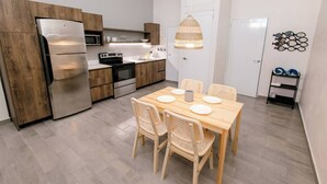 A modern kitchen with wooden cabinets, stainless steel appliances, and a dining area with wicker chairs and a wooden table.