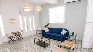 A living room with a blue sofa, two wicker chairs, a glass coffee table, and patterned floor tiles.