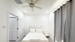 A bedroom with a bed, a nightstand, a ceiling fan, and a door. - Charming Apartment in Gorgeous George Town with GYM, Pool, and Pickleball Court (George Town)