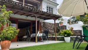 Une terrasse avec une table et des chaises, un espace abrité et des plantes en pot.