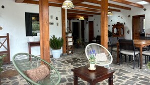 Un vaste espace intérieur doté d’un sol en pierre, de poutres en bois au plafond et d’un coin salon comprenant un fauteuil en osier et une table.