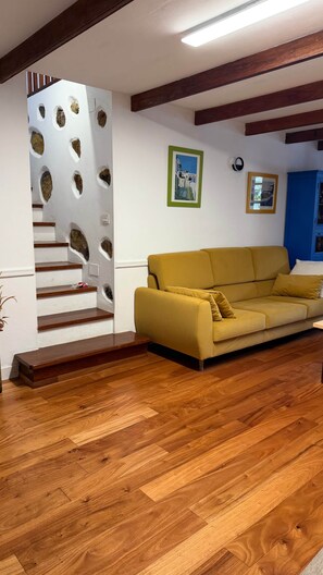 A living room with a wooden staircase, a yellow sofa, and wooden flooring.