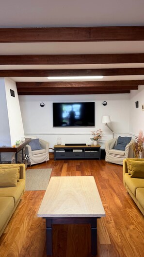 A modern living room with a flat-screen TV mounted on the wall, a wooden coffee table, and two sofas.