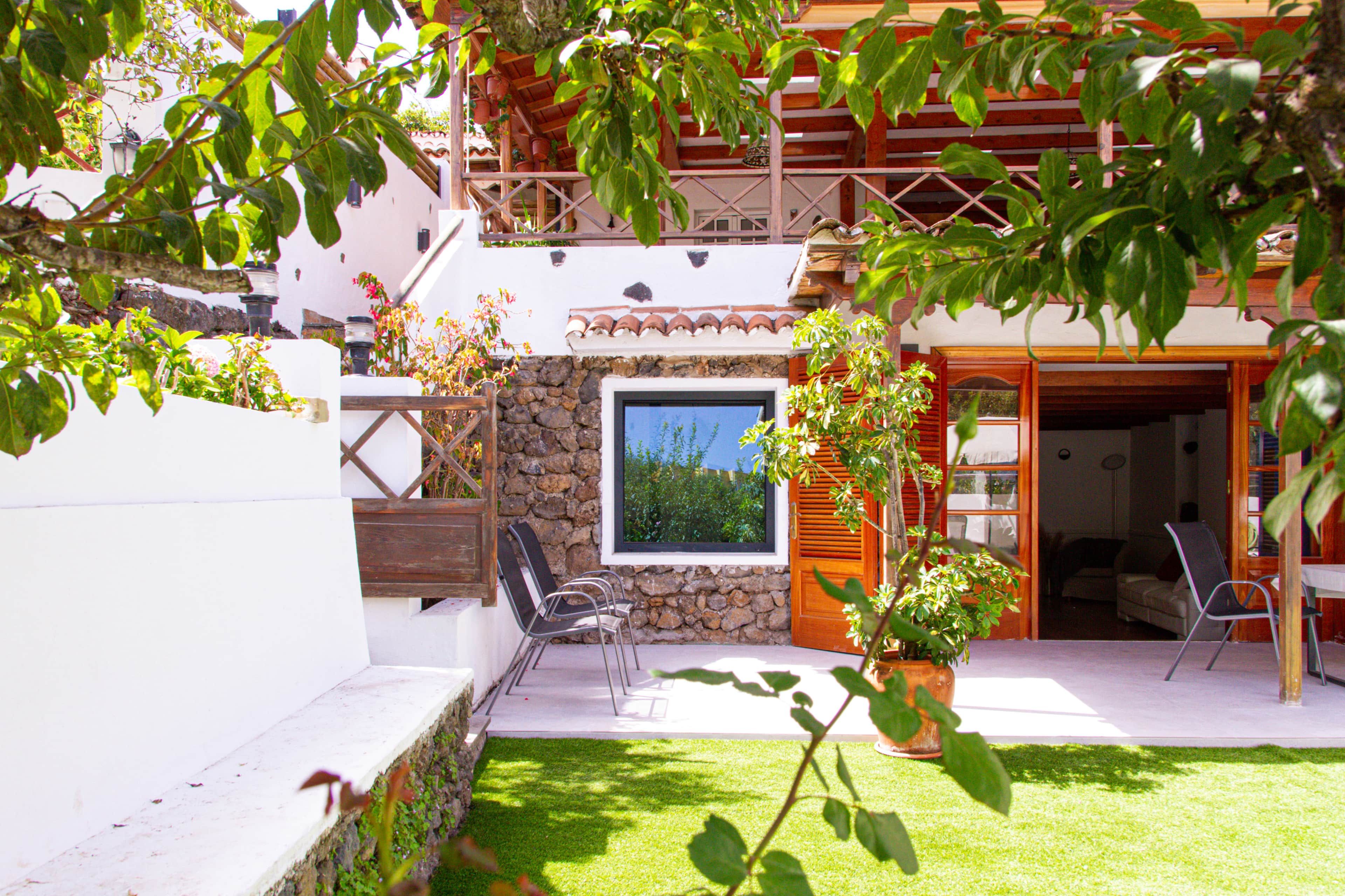 A courtyard with a stone wall, a wooden door, and a window overlooking greenery.