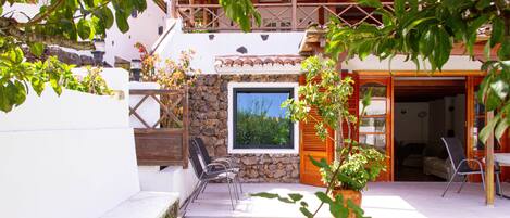 A courtyard with a stone wall, a wooden door, and a window overlooking greenery.