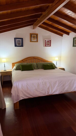 A bedroom with a wooden ceiling, a bed with white bedding, green pillows, and two bedside lamps.