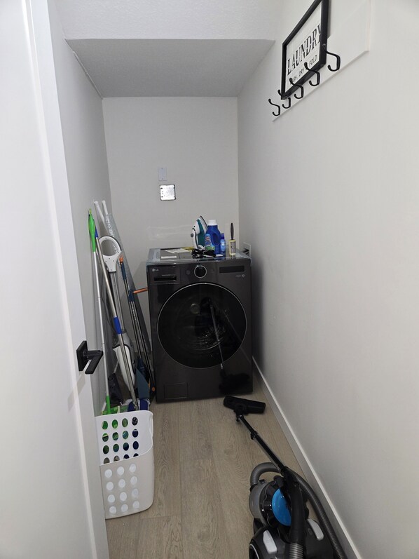 A laundry room with a washing machine, a drying rack, and a vacuum cleaner.