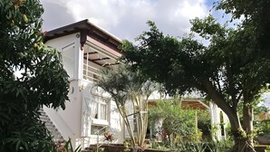 A white building with a red roof, surrounded by lush greenery and a variety of plants.