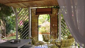 An outdoor patio with picnic tables and wicker chairs, surrounded by a bamboo fence and greenery.