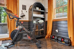 A stationary bike, a shelf with folded towels, and a set of dumbbells. - Family Retreat • Sauna • Hot Tub • Games • Peloton (Bartlett)